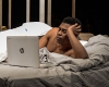 Actor laying in bed while looking at a laptop